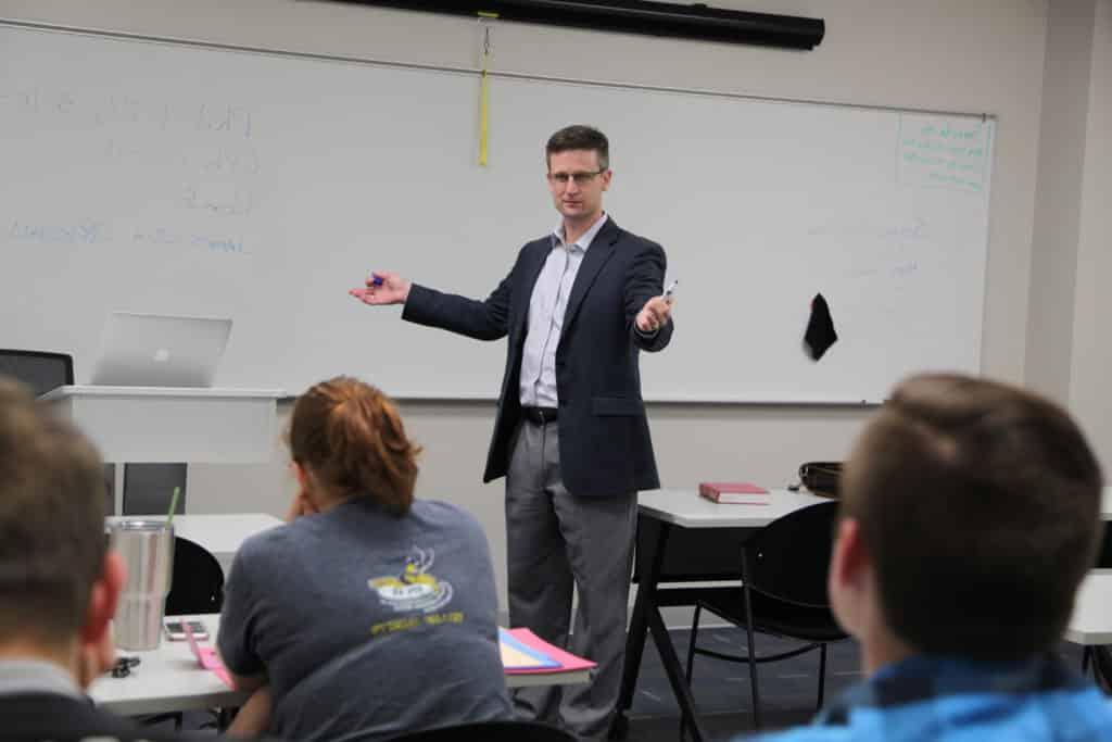 A Howard Payne University teacher gesturing while speaking to a classroom of students. | HPU